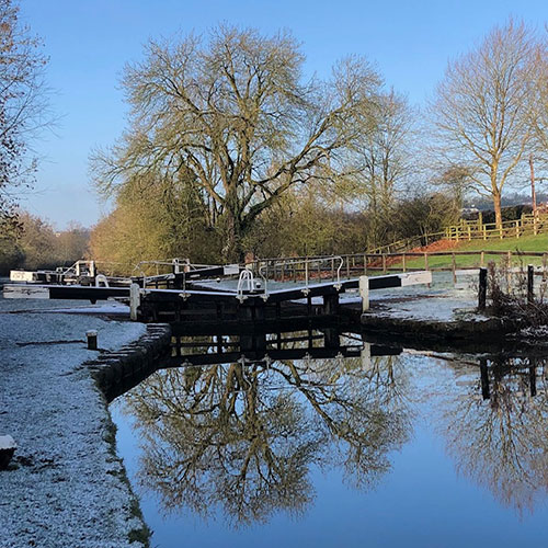 View of a lock with frost on the ground and a tree starting to come into leaf in the background