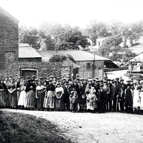 Old black and white photograph of a group of people standing outside some brick buildings in the 1920s
